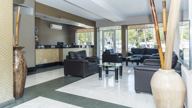 A modern lobby with a reception desk, seating area, and large windows. - Hotel Gran Via (Veracruz)