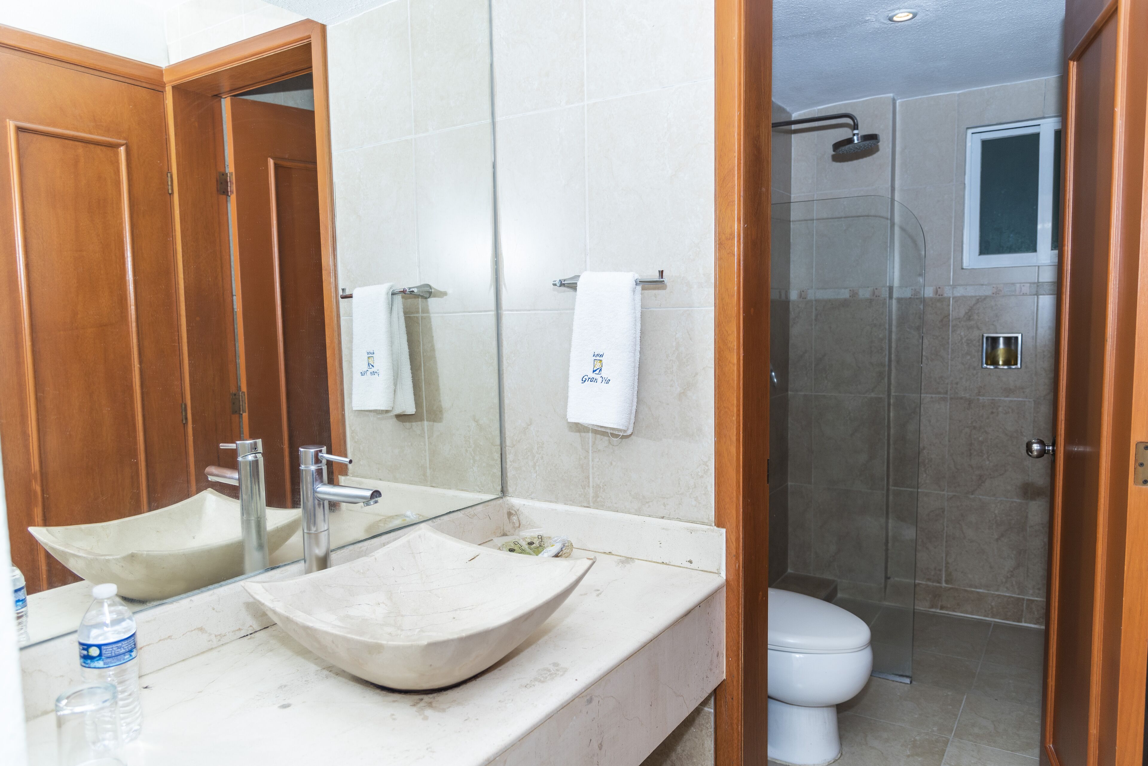 Une salle de bain avec un grand miroir, deux lavabos, des toilettes et un espace douche.