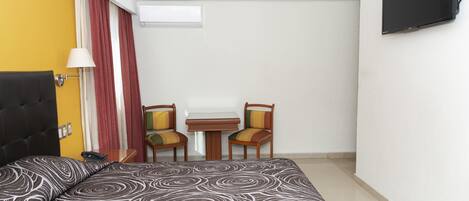 A hotel room with a bed, a desk, two chairs, a TV, and a window with curtains.