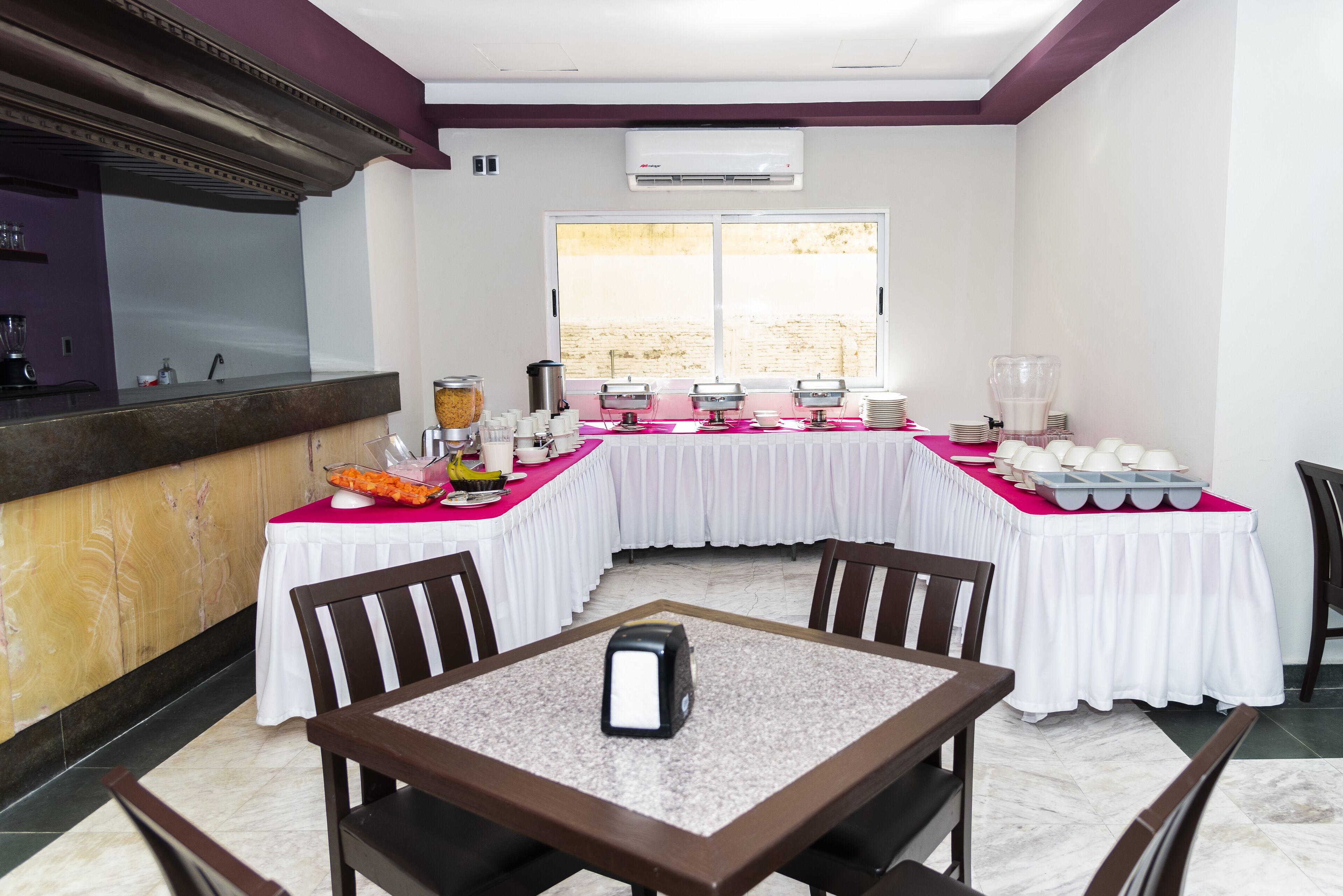 A dining area with a long table covered in white tablecloths, equipped with various food dispensers and a coffee machine.