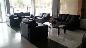 A modern living room with black leather sofas, a glass coffee table, and a view of the outdoors through large windows. - Hotel Gran Via (Veracruz)