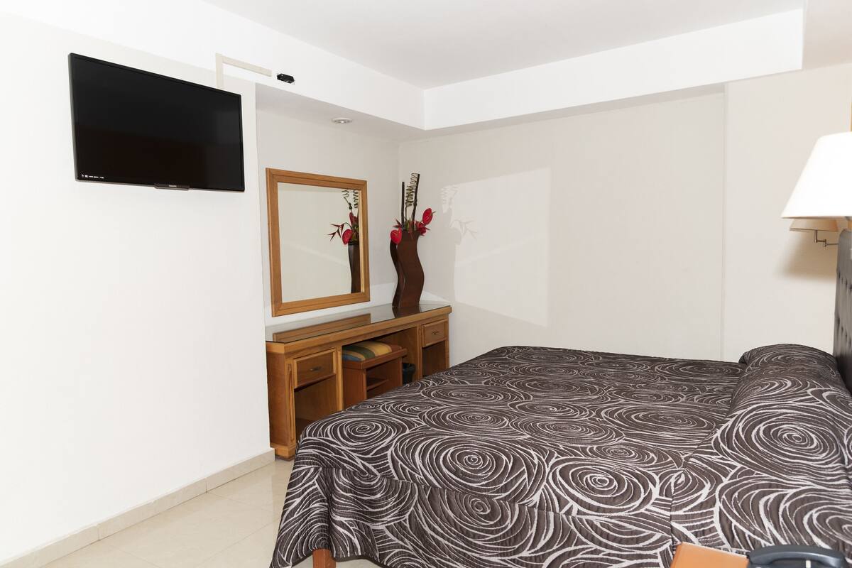 A bedroom with a bed, a dresser, a mirror, and a TV.