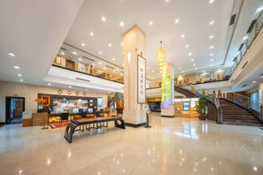 Eine großzügige Lobby mit hoher Decke, einer zentralen Säule und einer Treppe, die in eine obere Etage führt.