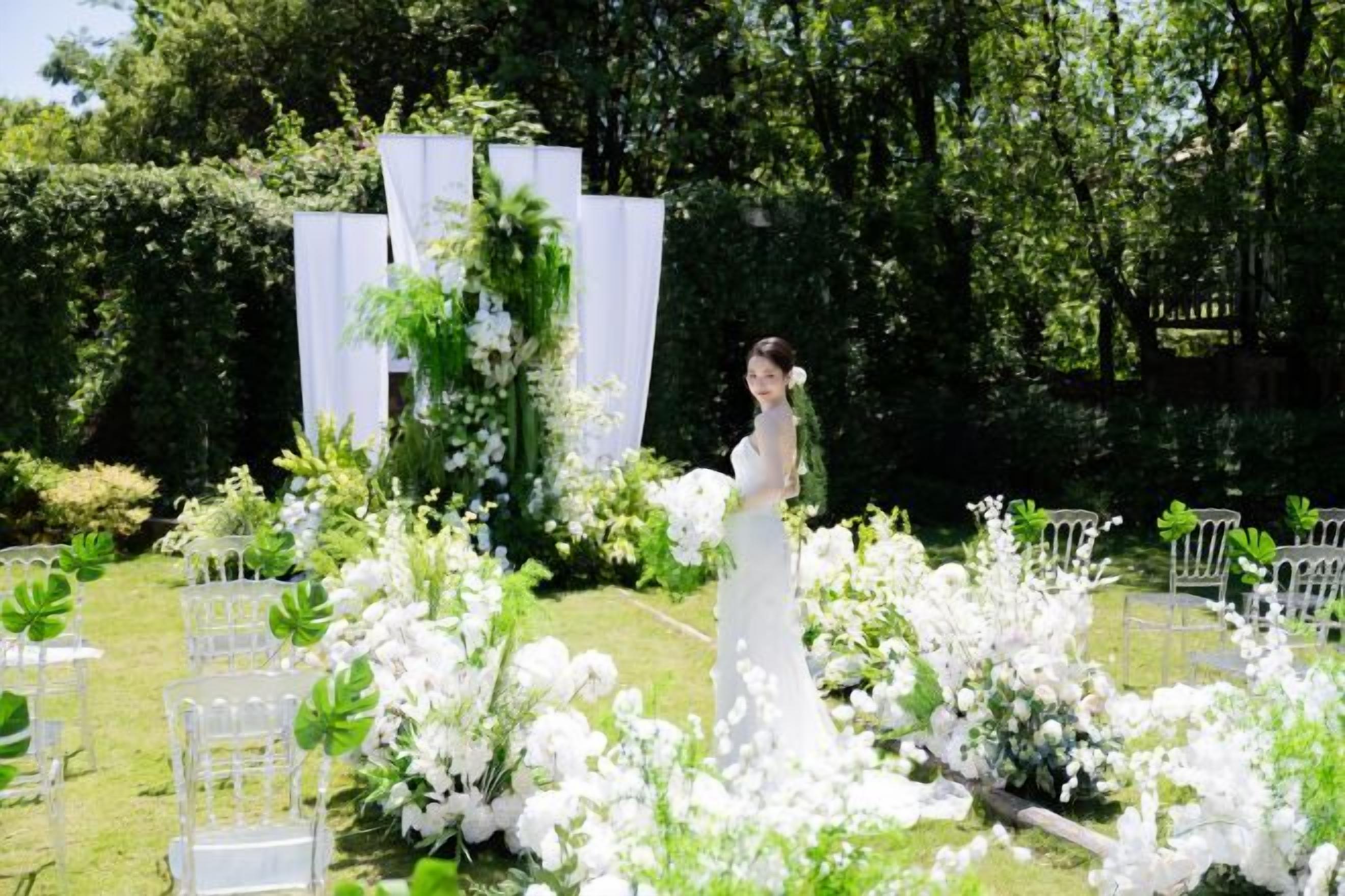 A wedding ceremony with a bride in a white dress, surrounded by white flowers and greenery.