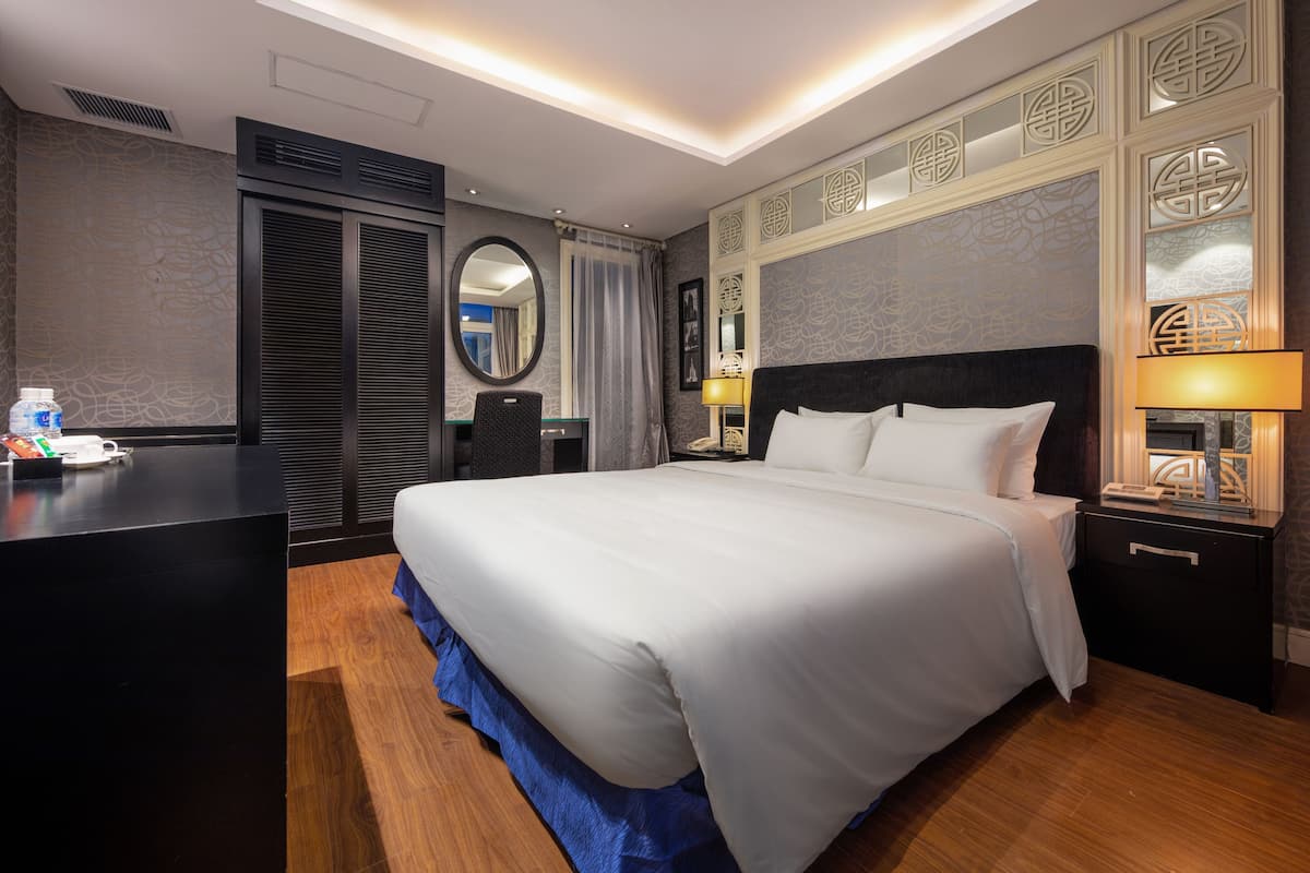 Habitació d'hotel amb un llit gran, una taula de treball, una cadira i una tauleta de nit amb una làmpada.