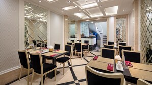 A hotel dining area with multiple tables and chairs, a central counter, and a staircase in the background. - Classy Boutique Hotel (Hanoi)