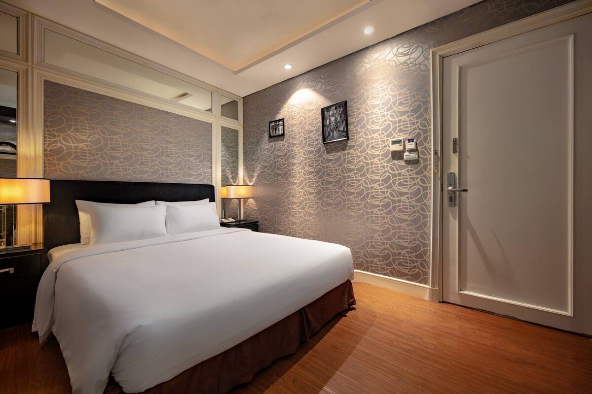 Habitació d'hotel amb un llit gran, dues làmpades de nit, un mirall i una porta.