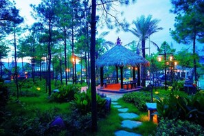 A thatched-roof gazebo surrounded by lush greenery and stone pathways.