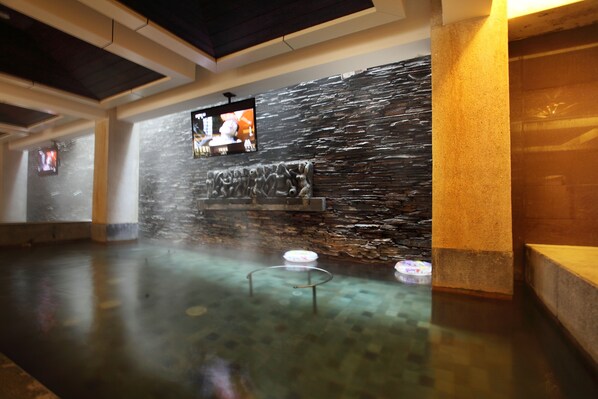 A spa area with a stone wall, a television, and a hot tub.
