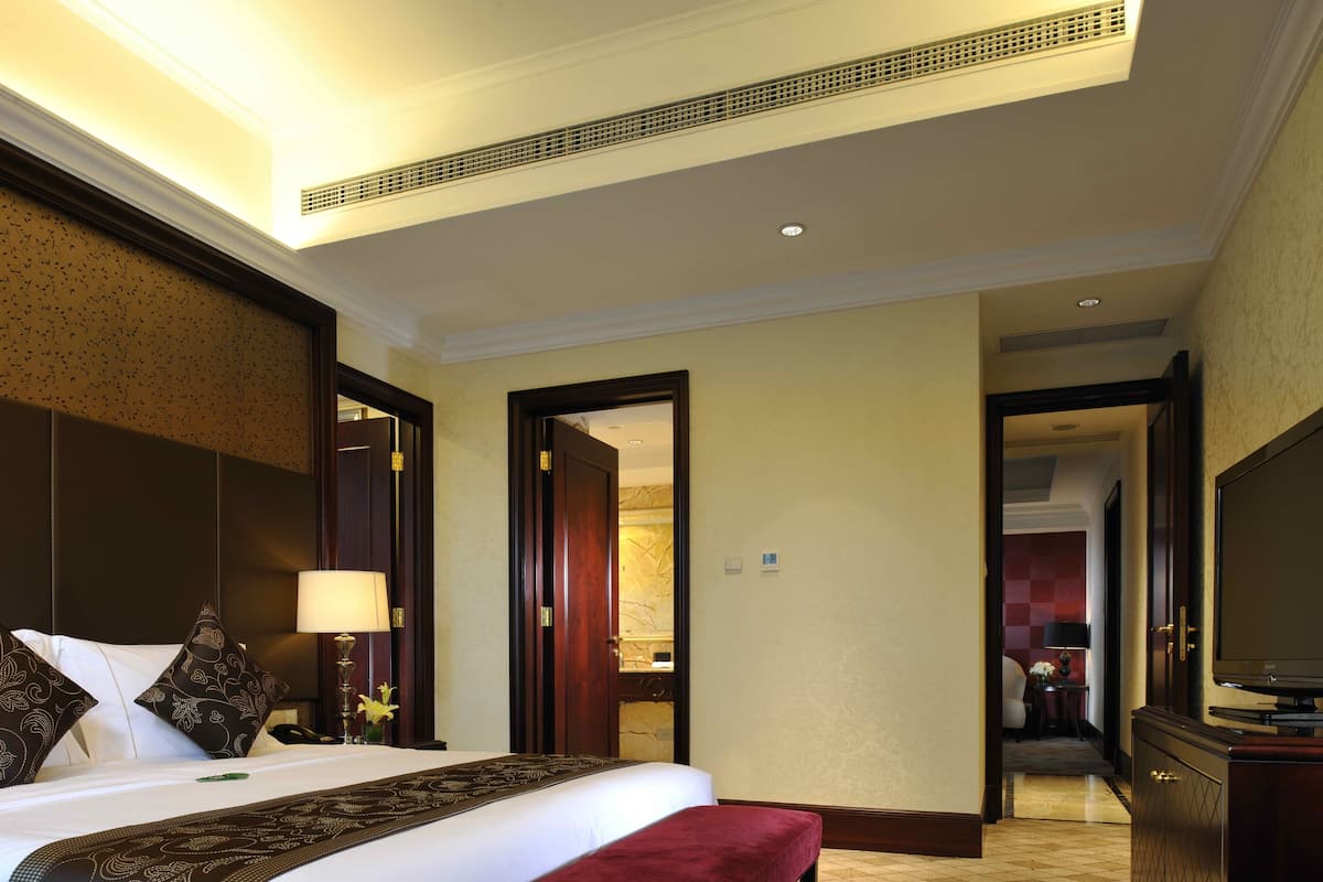 A hotel room with a large bed, a bench, a TV, and a bathroom visible through an open door.