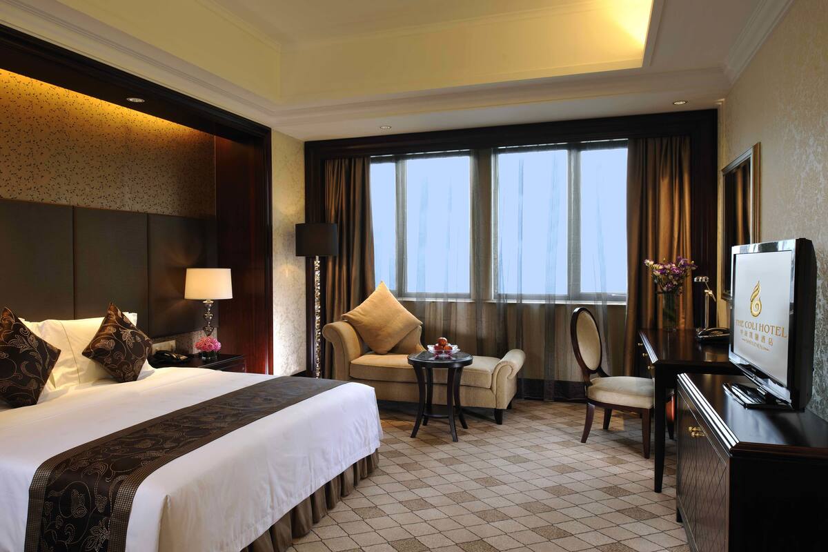 A hotel room with a large bed, a sofa, a desk, and a TV.