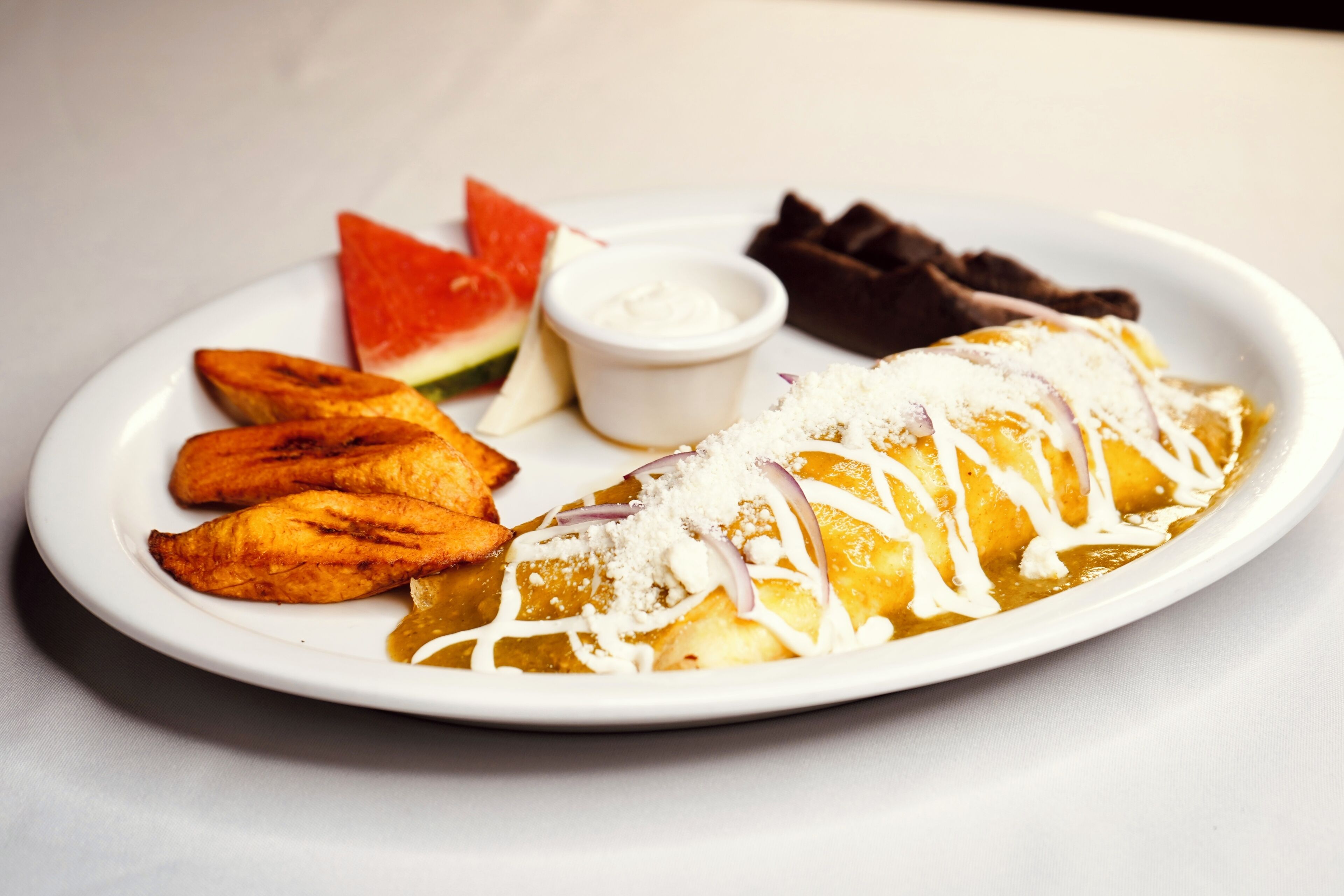 A plate with a rolled dish, a small bowl of sauce, and a piece of chocolate.