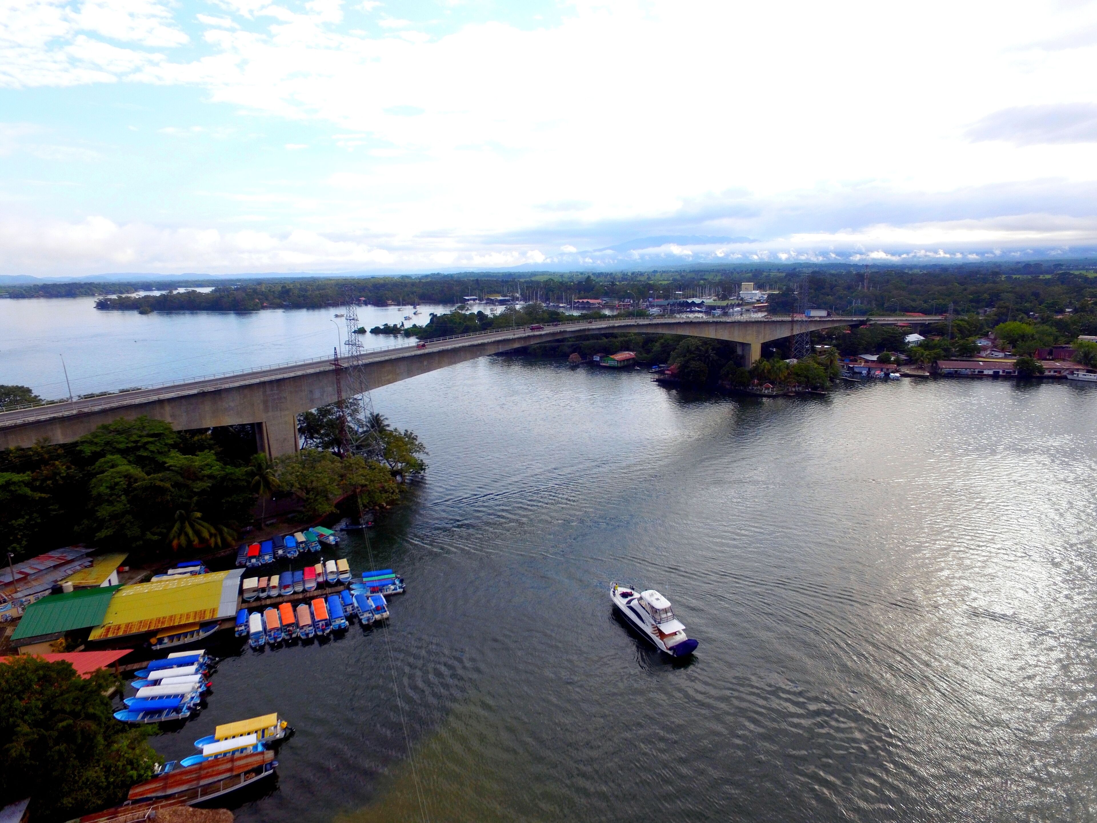 A river with a bridge, boats, and a dock with colorful canopies.