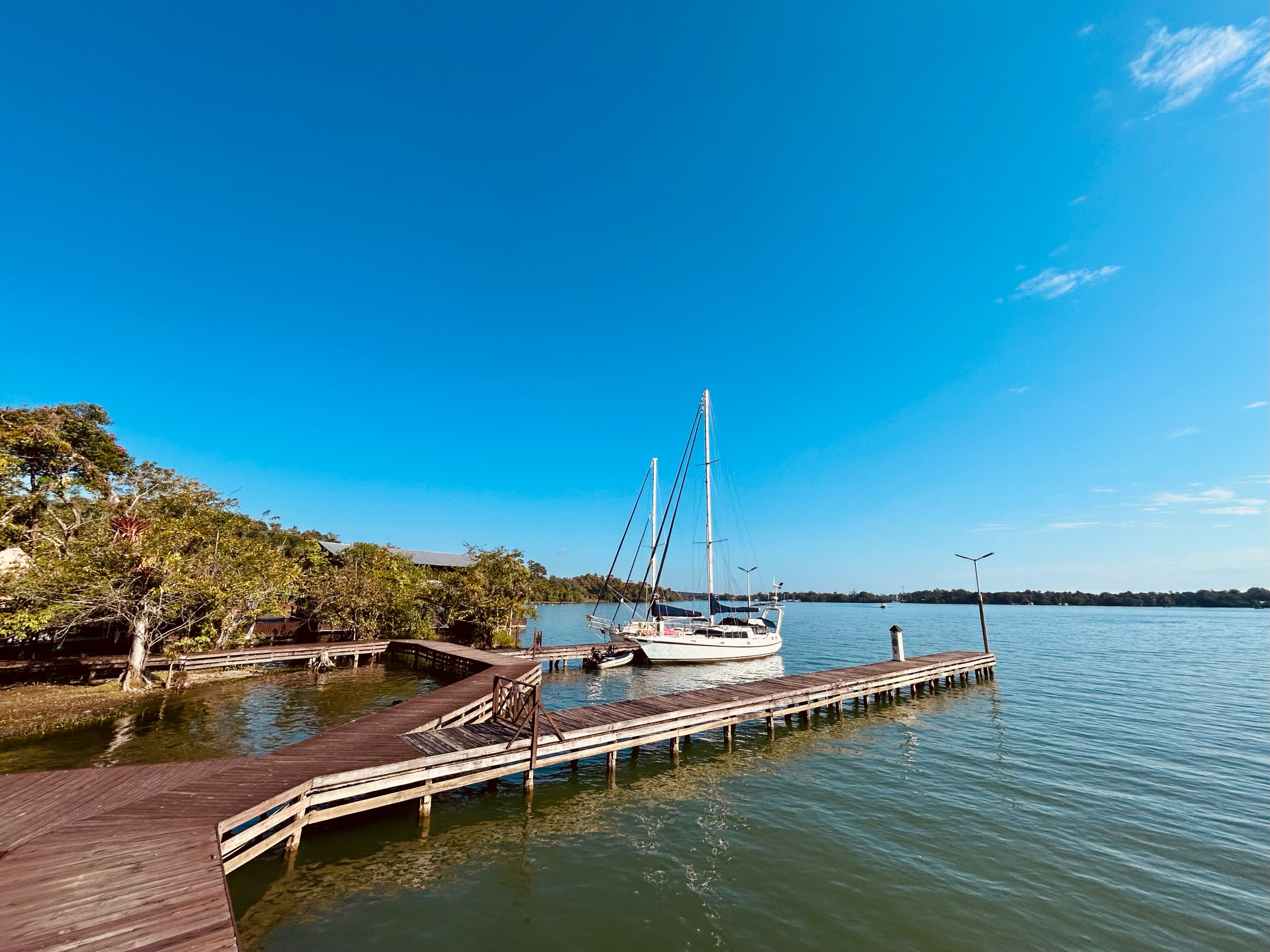 A wooden dock extending into calm water with a sailboat moored at the end.