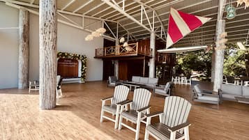 A spacious indoor area with wooden flooring, several chairs, a large flag, and a wooden structure with a balcony.