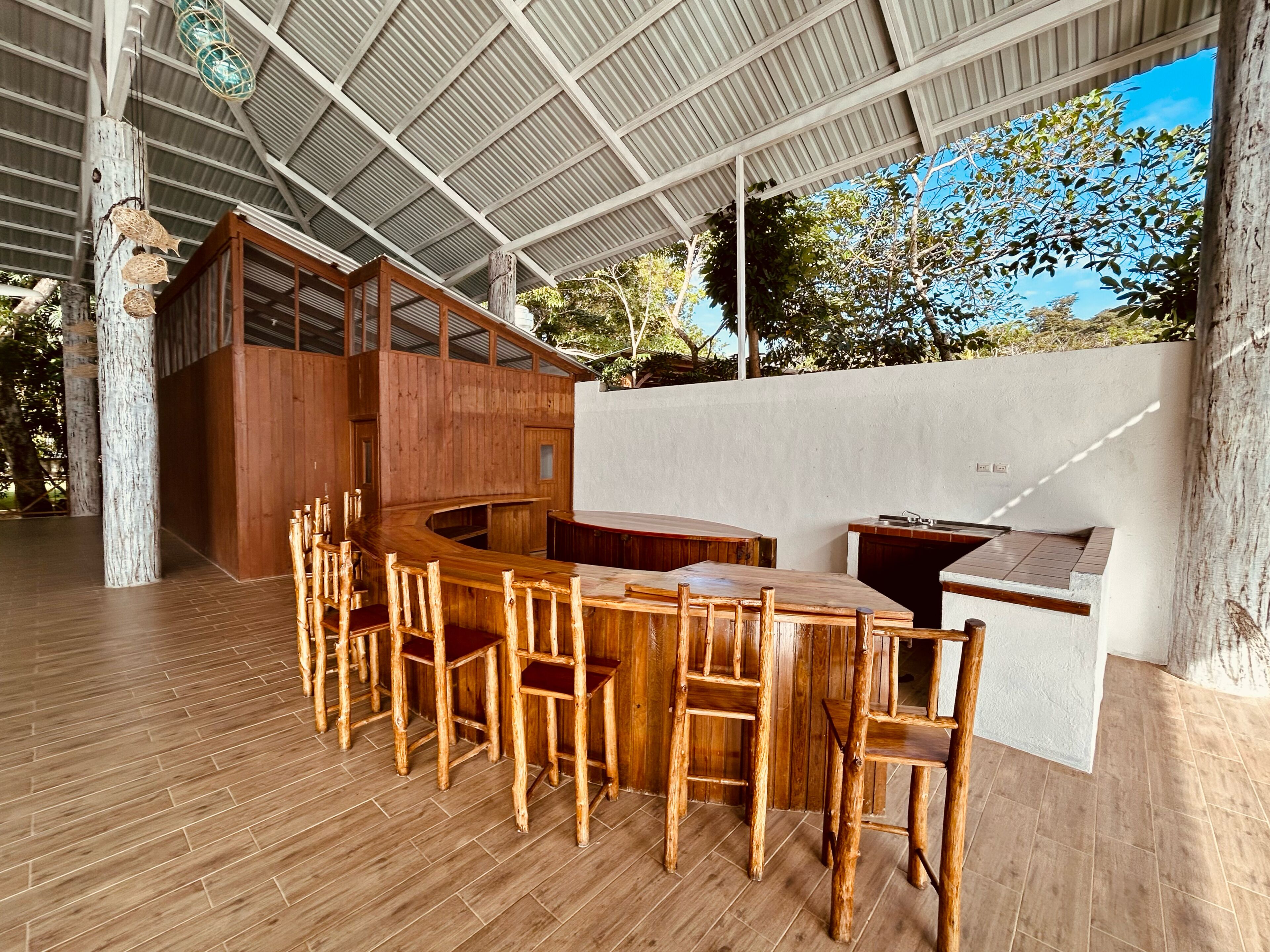 Un comedor de madera con un banco curvo y sillas, una estación de parrilla empotrada y un techo de metal corrugado a techo alto.