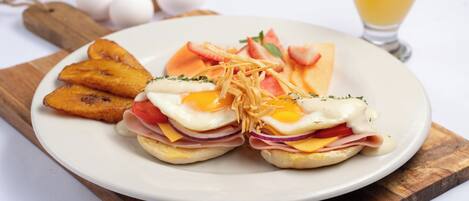 A plate with eggs, ham, cheese, and tomatoes, accompanied by fried plantains and a glass of orange juice.