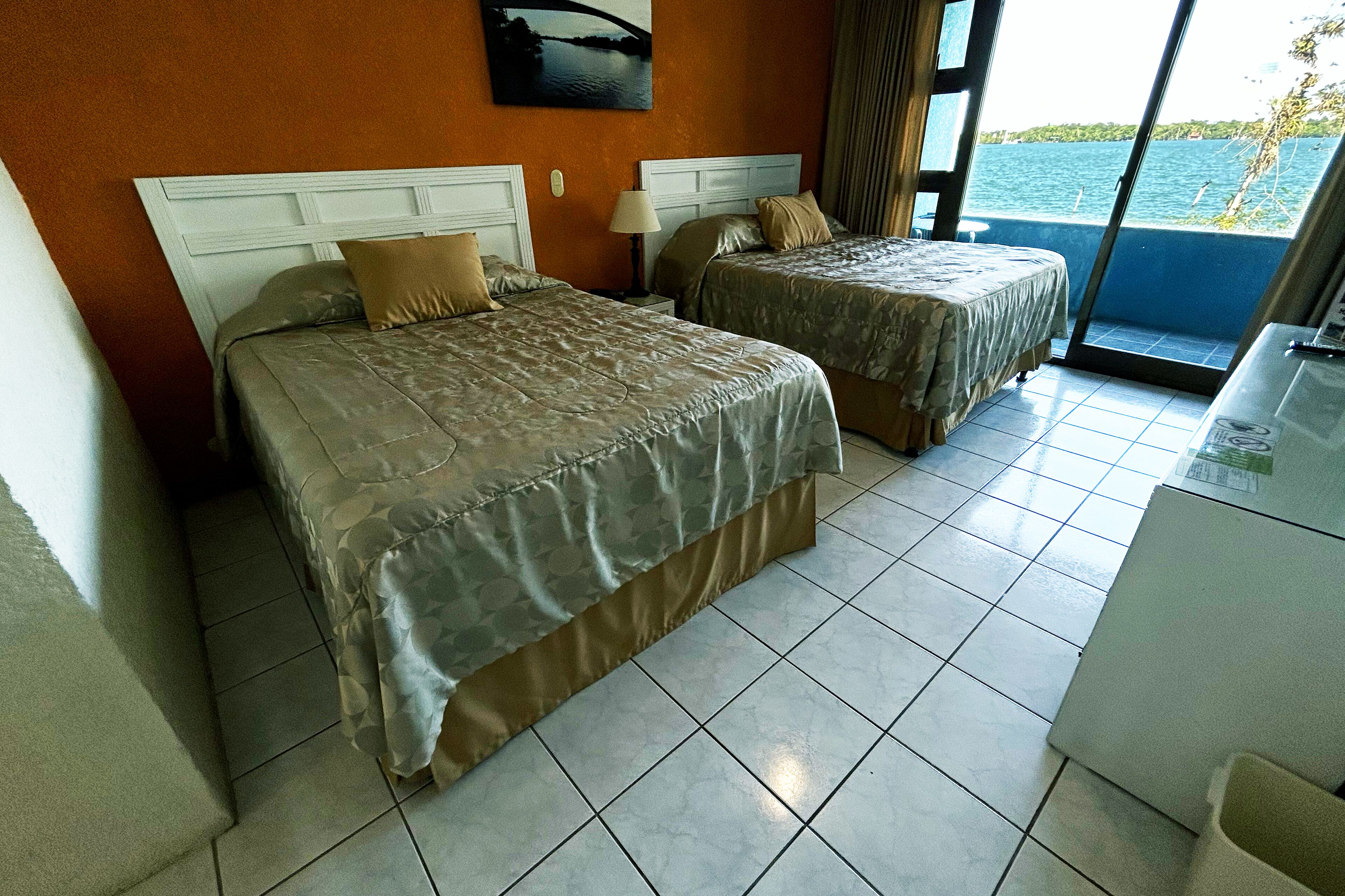 A hotel room with two beds, a desk, and a view of the sea.