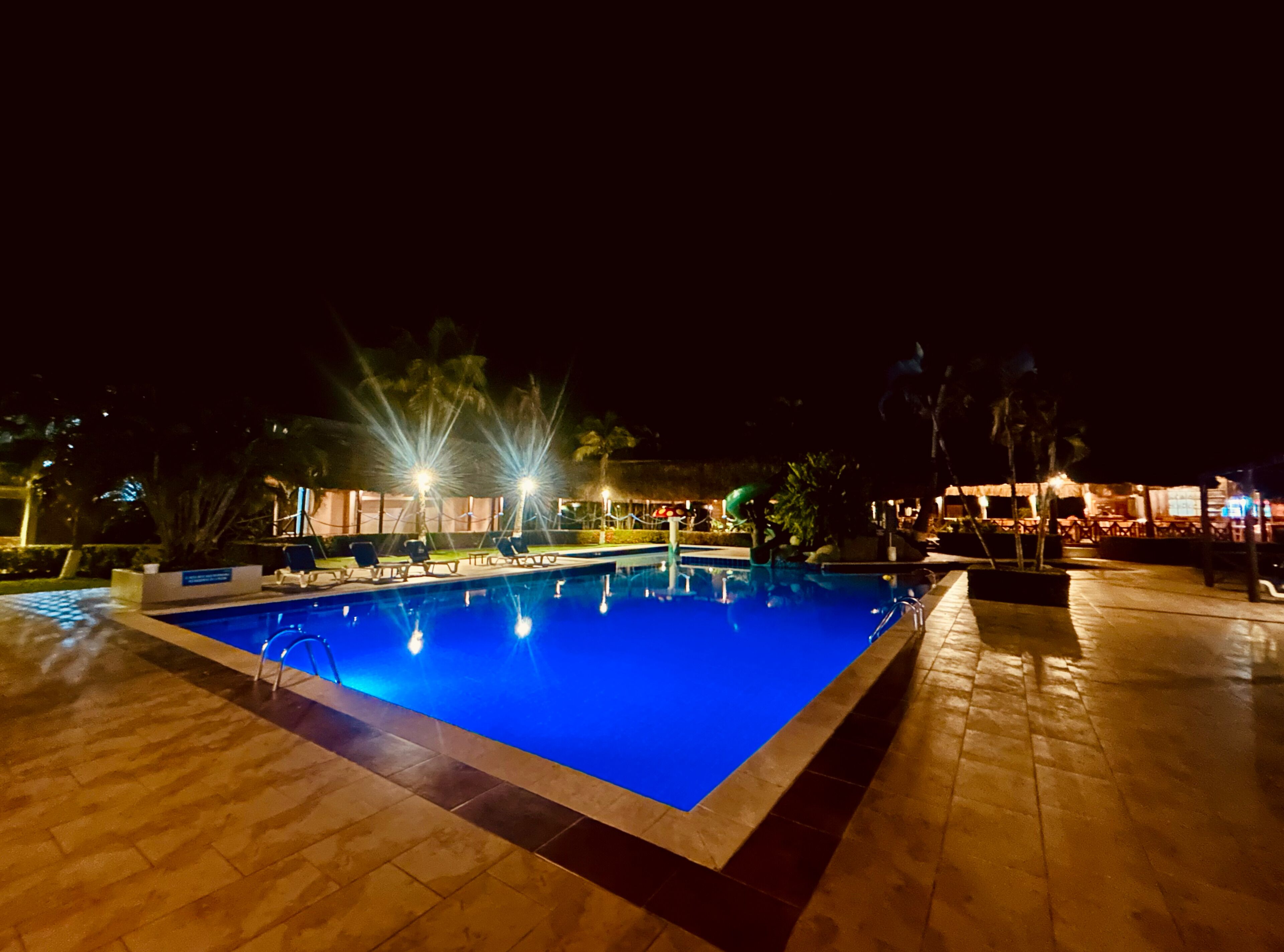 Una piscina iluminada de noche con sillas de descanso.