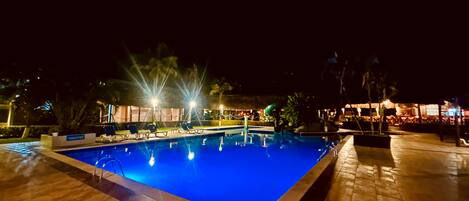 Una piscina iluminada de noche con sillas de descanso.