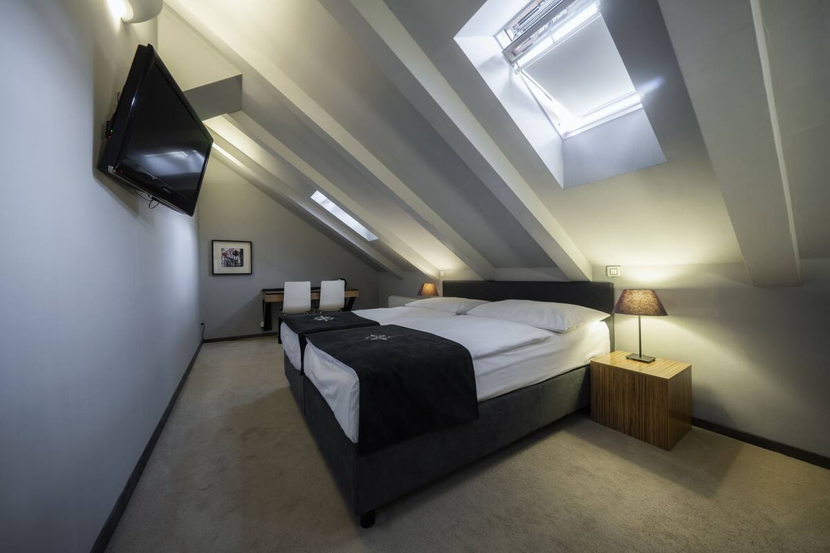 A modern bedroom with a bed, bedside tables, a TV mounted on the wall, and a skylight.