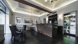 A modern lobby with a marble reception desk, dark wood flooring, and a chandelier. - Hotel Noir (Prague)