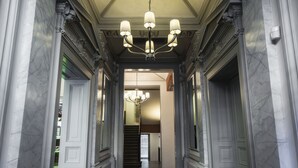 A grand hallway with marble walls, a chandelier, and a staircase leading to another level. - Hotel Noir (Prague)