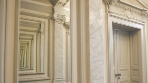 A hallway with ornate moldings, a marble wall, and a door with a classic design. - Hotel Noir (Prague)