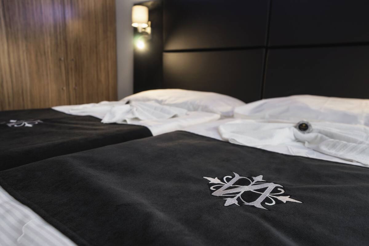 Habitación de hotel con dos camas, cada una con una colcha negra y una almohada blanca.