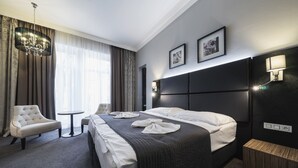 A hotel room with a large bed, a chair, a small table, and a chandelier. - Hotel Noir (Prague)