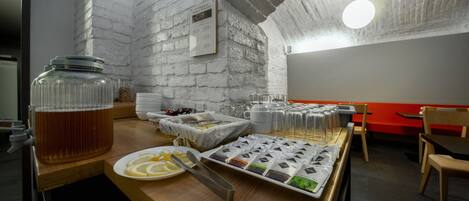 A breakfast buffet setup with a variety of food items and beverages, a large jar of tea, and a wall-mounted menu.