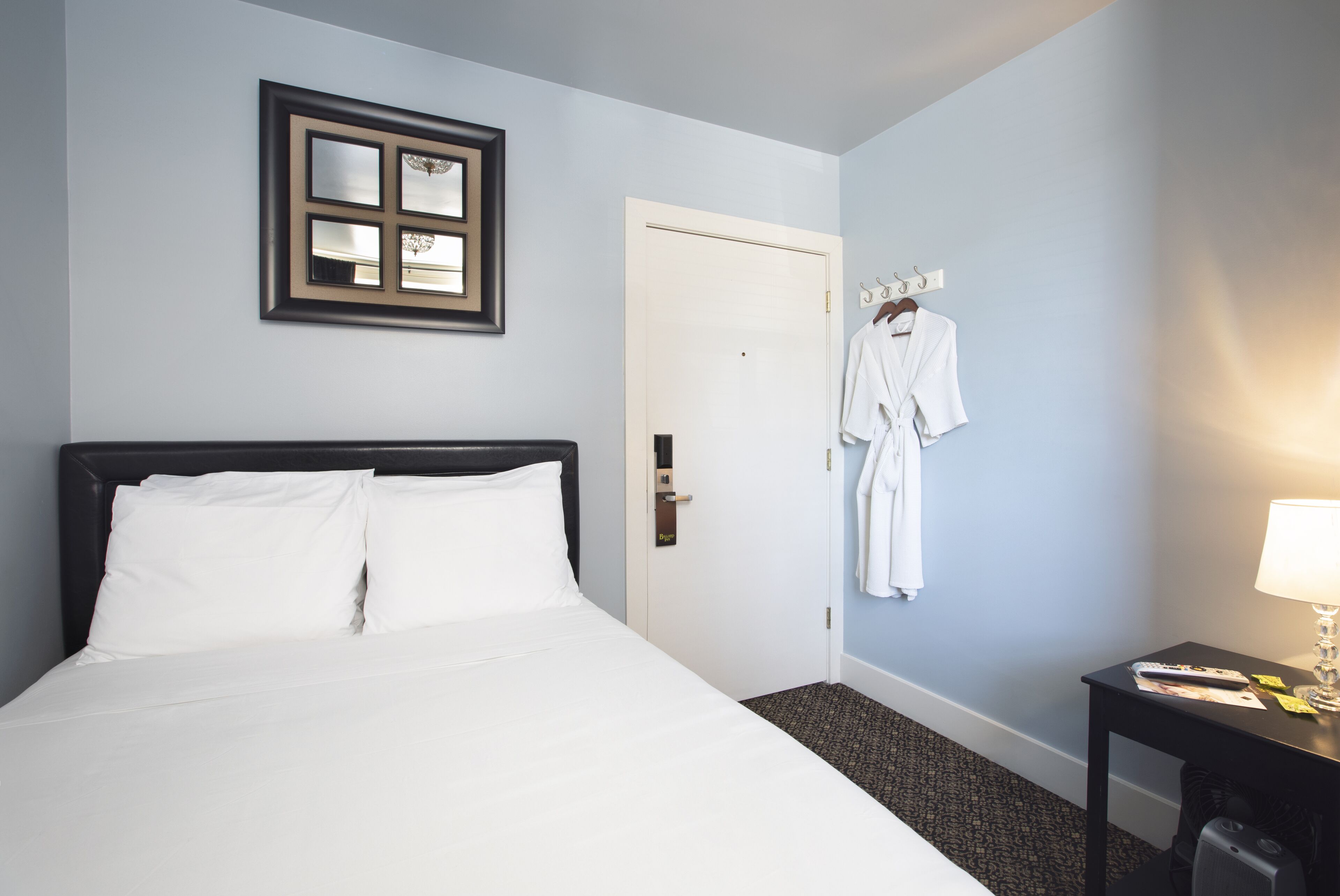 Une chambre d’hôtel avec un lit, une armoire, un miroir et une table avec une lampe.