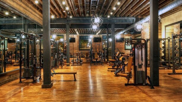 A gym with wooden floors, exercise equipment, and large windows. - Ballard Inn (Seattle)