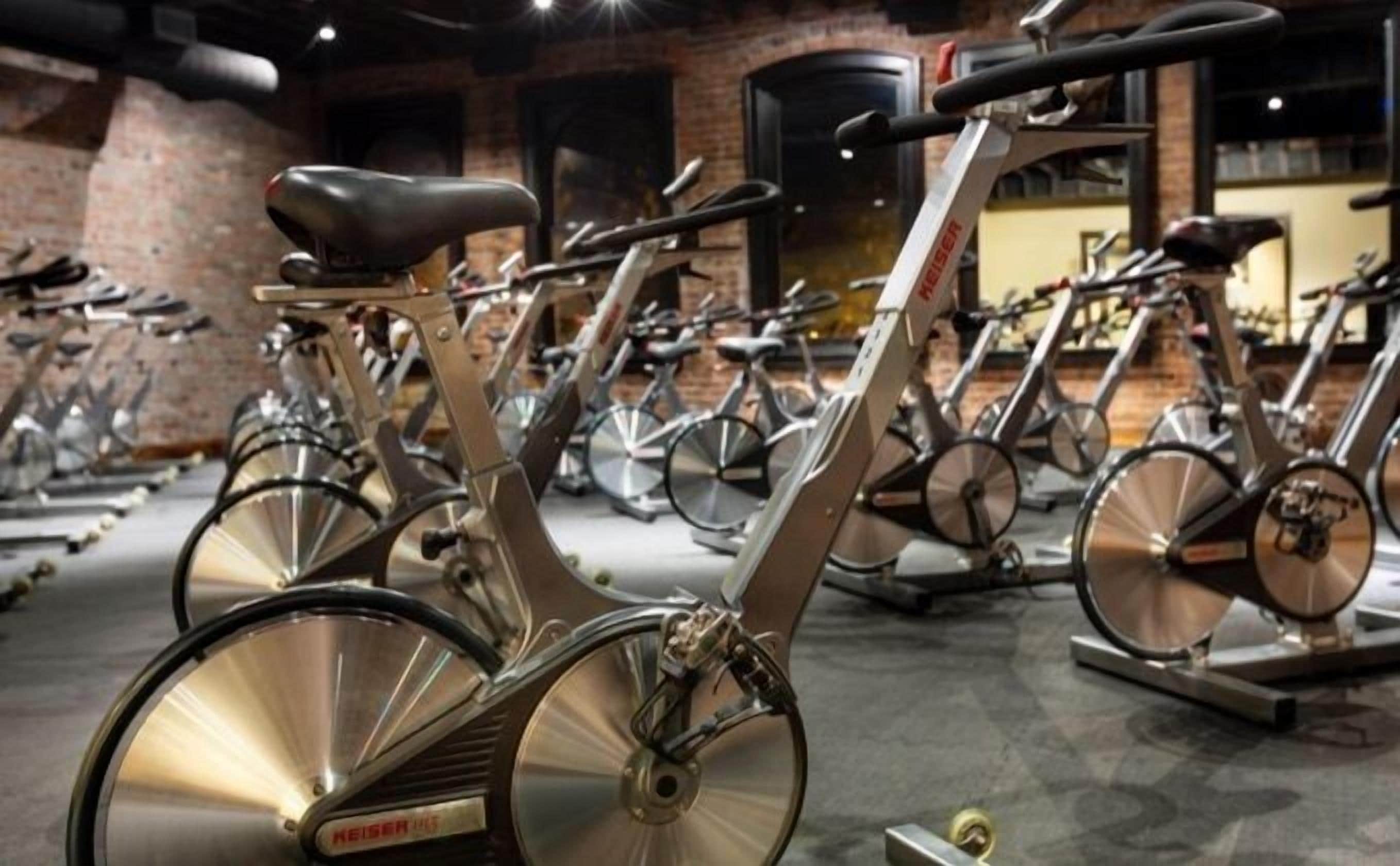 A row of stationary bikes in a gym with brick walls and a polished floor.