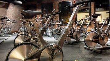 A row of stationary bikes in a gym with brick walls and a polished floor.
