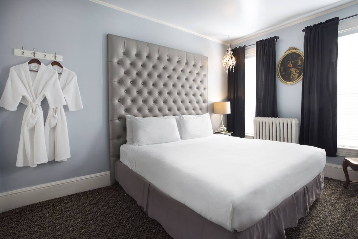 A neatly made bed in a hotel room with a tufted headboard, a bedside lamp, and a radiator.