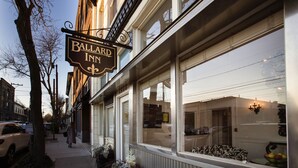 A storefront with a sign for Ballard Inn, featuring large windows and a visible interior with a sofa and fruit bowl. - Ballard Inn (Seattle)