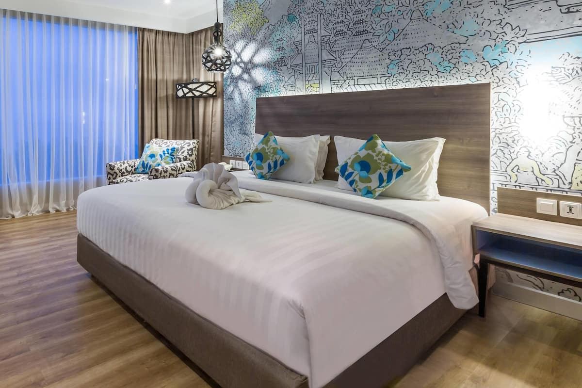 A neatly made bed with white linens and decorative pillows, a wooden headboard, a bedside table, and a patterned wall mural.