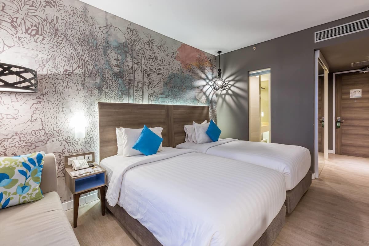 A hotel room with two beds, a nightstand with a phone, and a wall mural.
