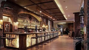 A bar area with a long counter, multiple stools, and a brick wall with shelves. - Wyndham Garden Kuta Beach, Bali (Kuta)