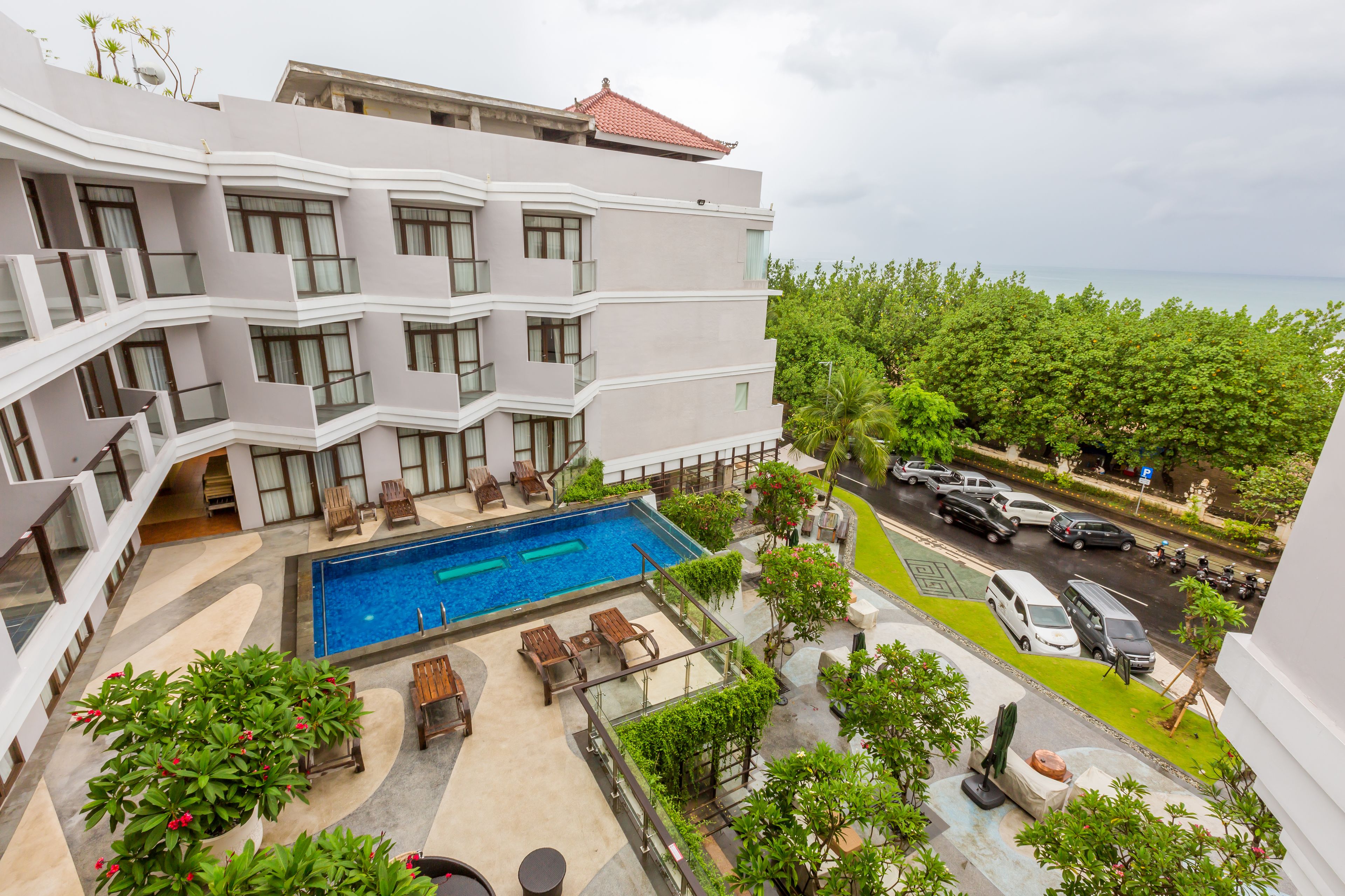 Un hotel de varios pisos con piscina en la azotea, zona de estar al aire libre y vistas al mar.