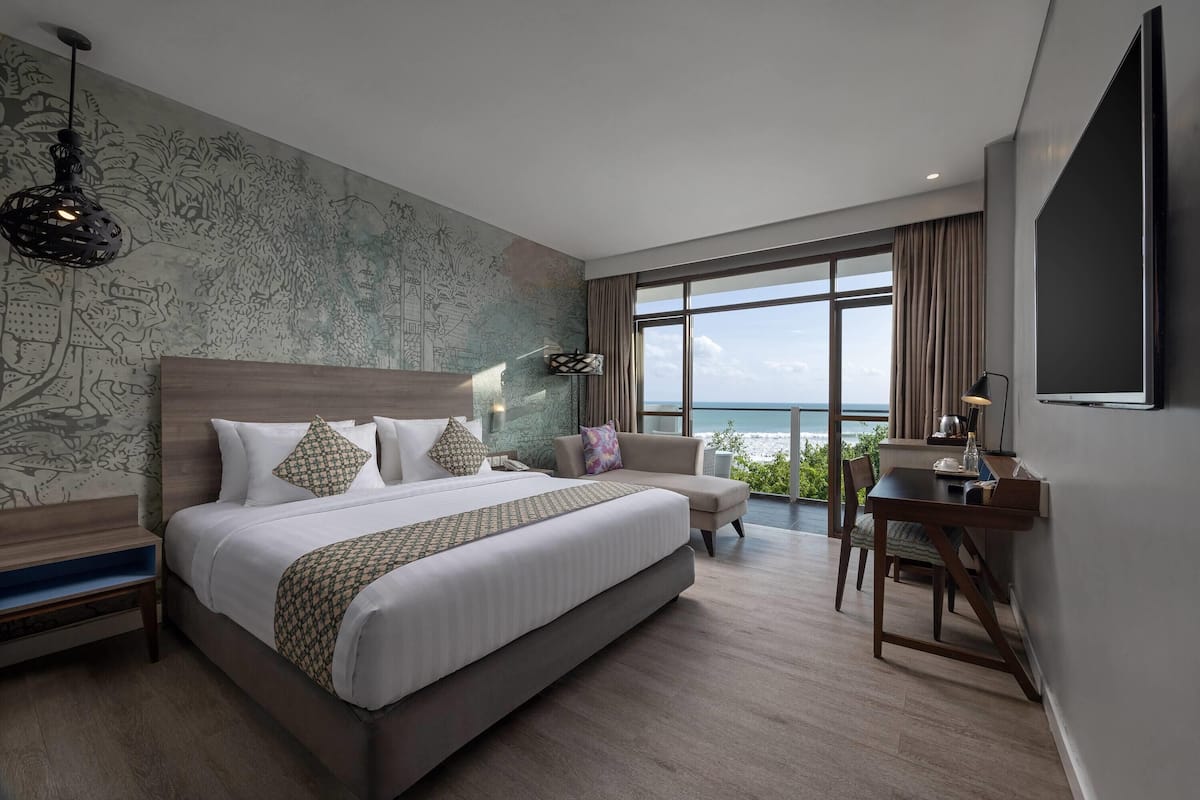 A modern hotel room with a large bed, a desk, and a view of the ocean.
