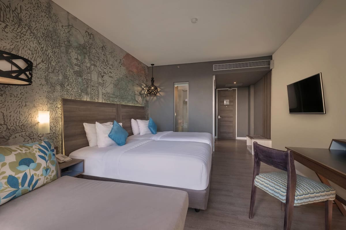 A hotel room with two beds, a desk, a chair, a TV, and a map mural on the wall.