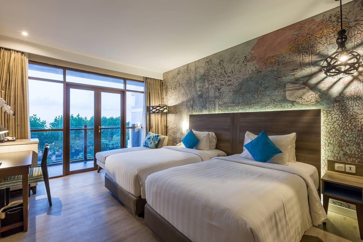 A hotel room with two beds, a desk, and a large window offering a view of the outdoors.