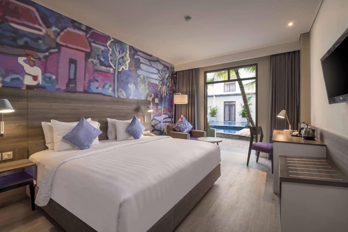 A hotel room with a large bed, a desk, a chair, and a TV.