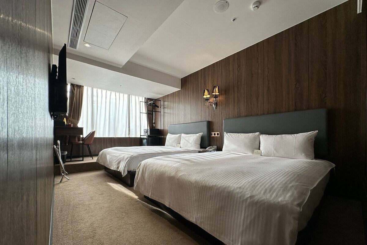 A hotel room with two beds, a desk, and a chair.