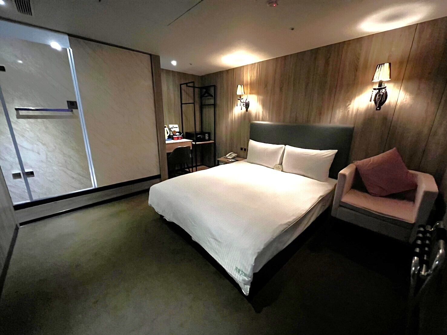A hotel room with a large bed, a desk with a chair, a wardrobe, and two wall-mounted lamps.