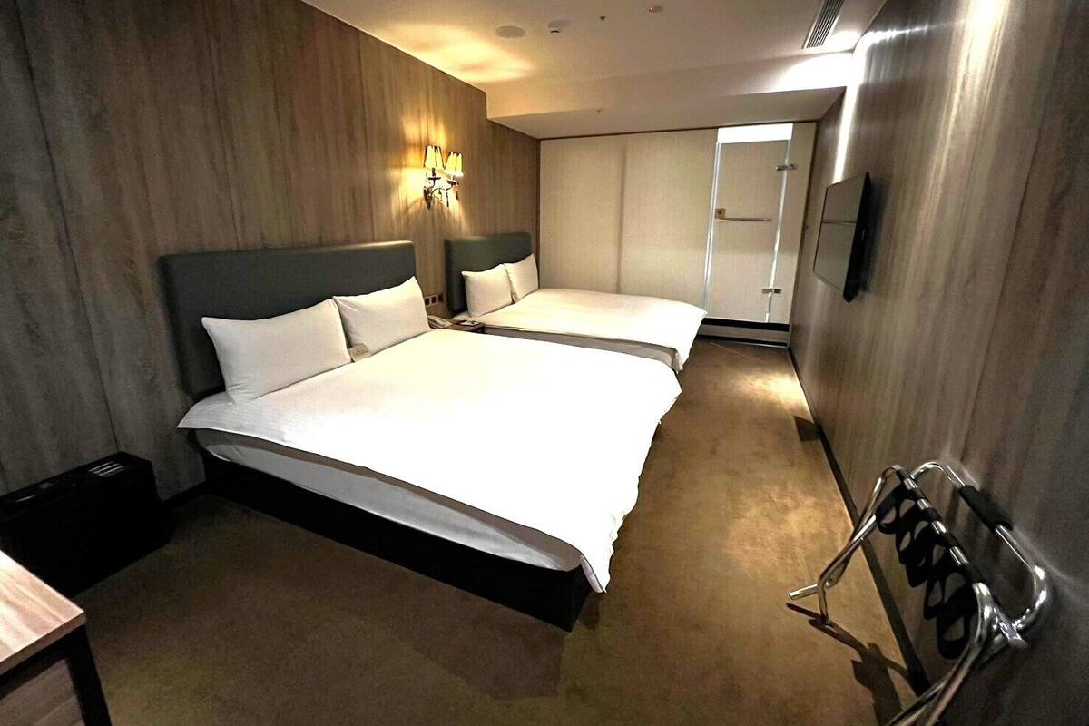A hotel room with two beds, a wall-mounted TV, and a shoe rack.