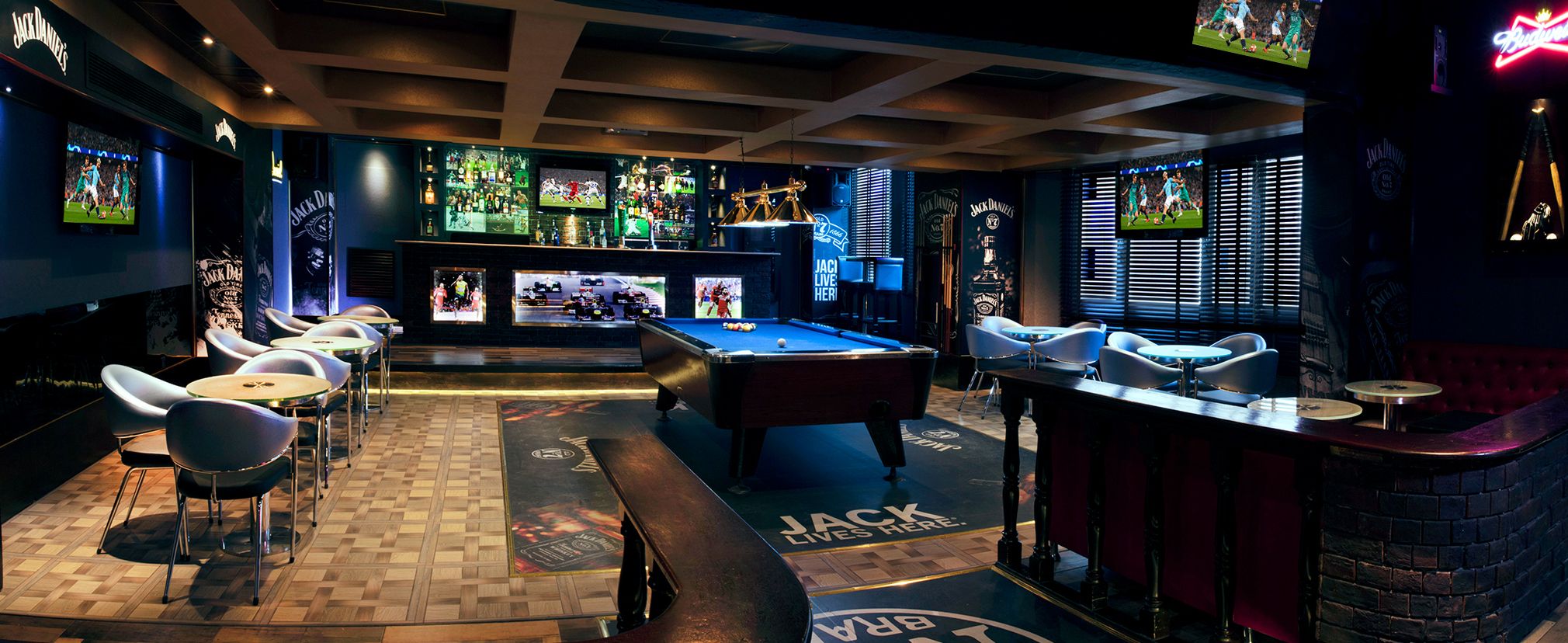 A bar area with a pool table, seating, and multiple screens displaying sports events.