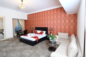 A hotel room with a large bed, a sofa, a dining area, and a patterned wall. - Grand Safir Hotel (Manama)